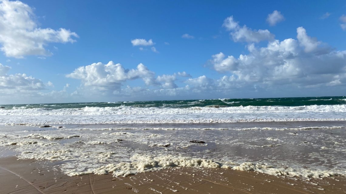 Petite vague écumeuse venant mourir sur le sable mouillé, vue face à la mer.