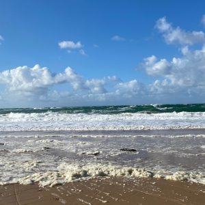 Petite vague écumeuse venant mourir sur le sable mouillé, vue face à la mer.